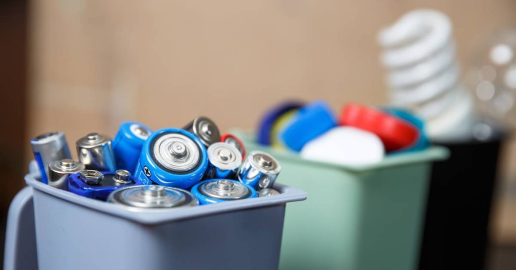Three small containers sit next to one another. The closest one is filled with various types of batteries.